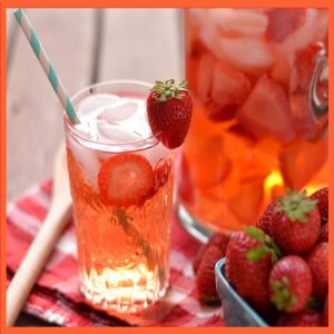 Glass of strawberry-infused Ayurvedic detox water with ice and fresh strawberries on a red checkered napkin.