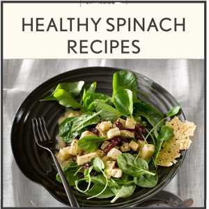 Healthy spinach salad with cheese cubes, cranberries, and parmesan crisp on a black plate